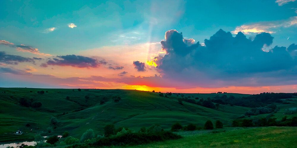 Sunset mural with dramatic sky and green meadow, ideal for indoor and outdoor spaces.